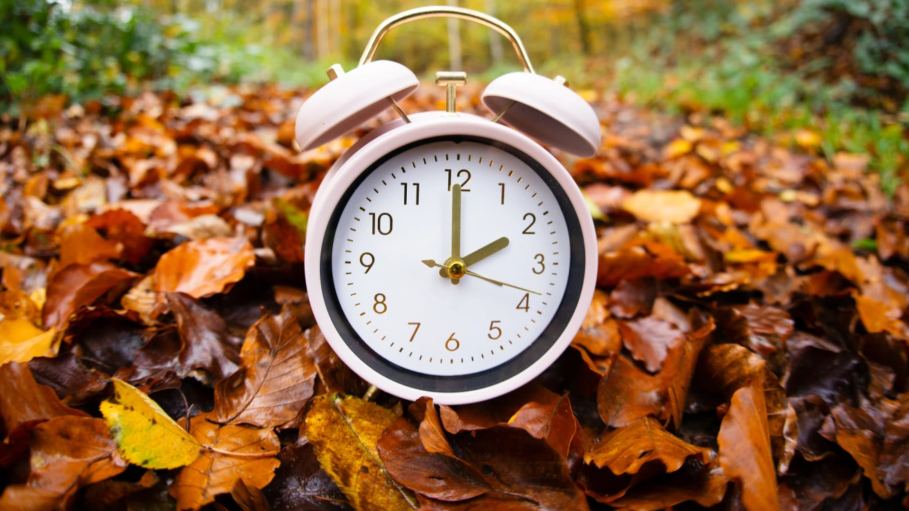 Reloj rodeado de hojas de otoño que ilustra el cambio de hora en Indiana en noviembre de 2026.